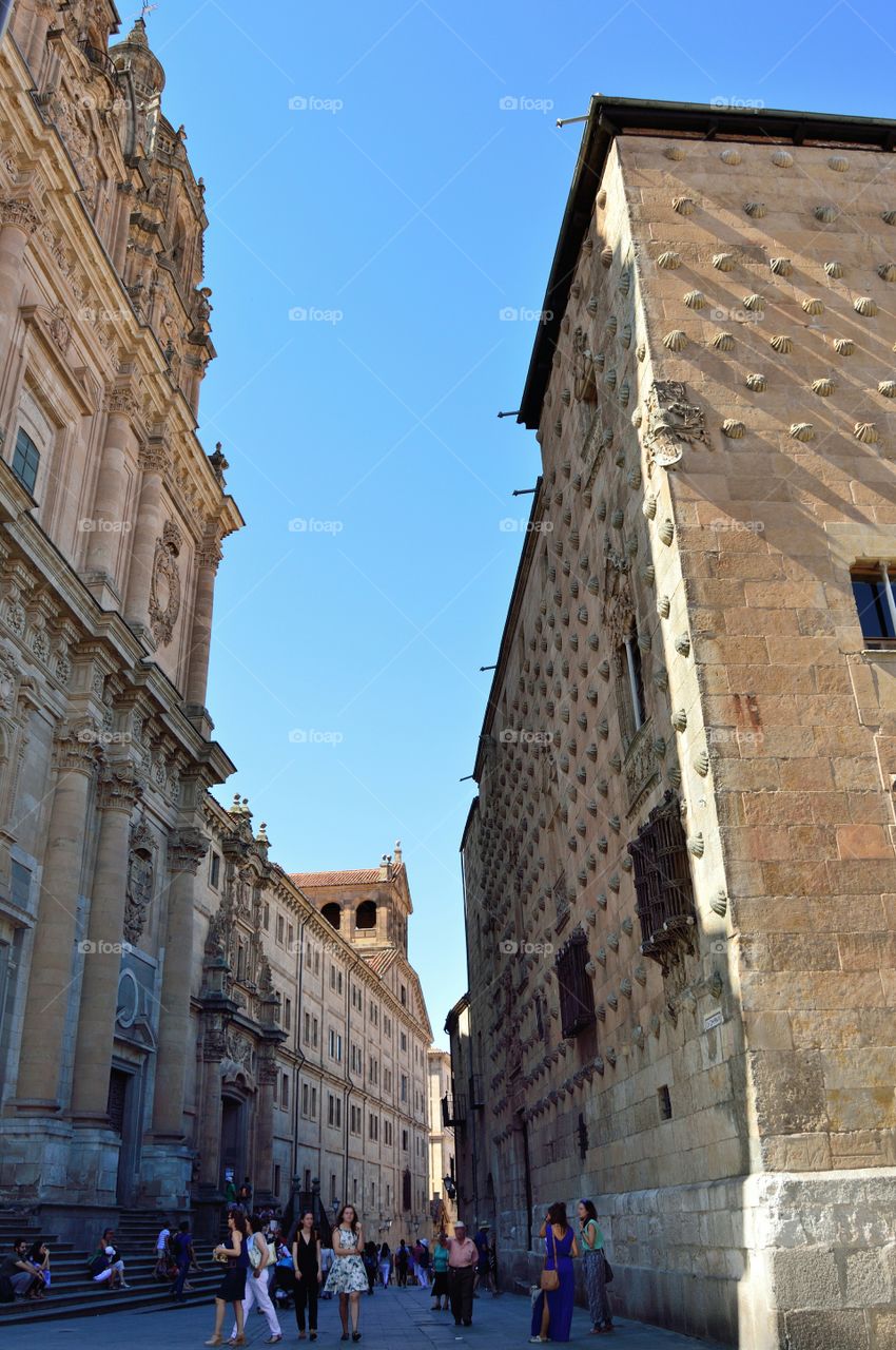 Walking in Salamanca. Building of the Pontifical University on the left and Casa de las Conchas on the right. Spain.