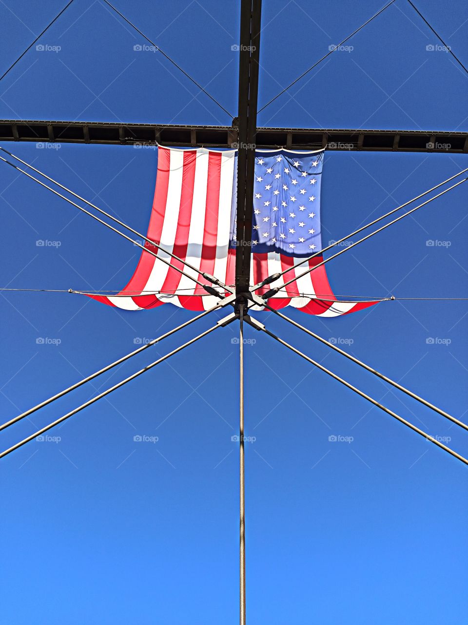 blue skies, American flag attached to a bridge.
