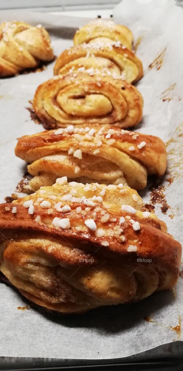 The fresh homemade rolled buns filled with sugar, cinnamon and butter on the baking paper.