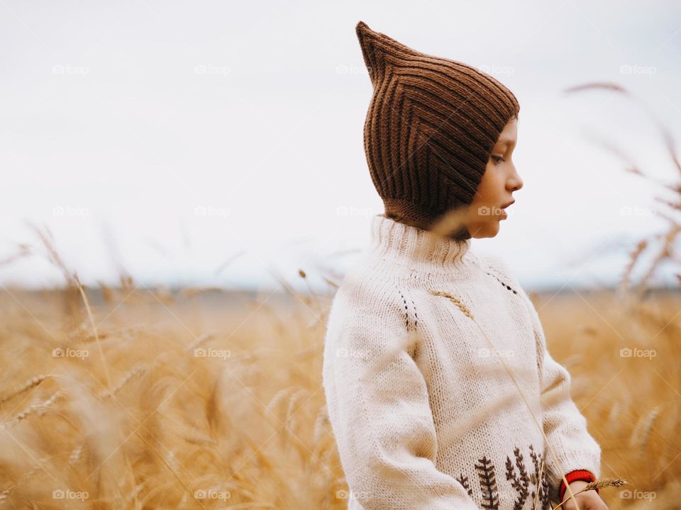 Cute little boy standing in the wheat field on the autumn day, portrait of child 