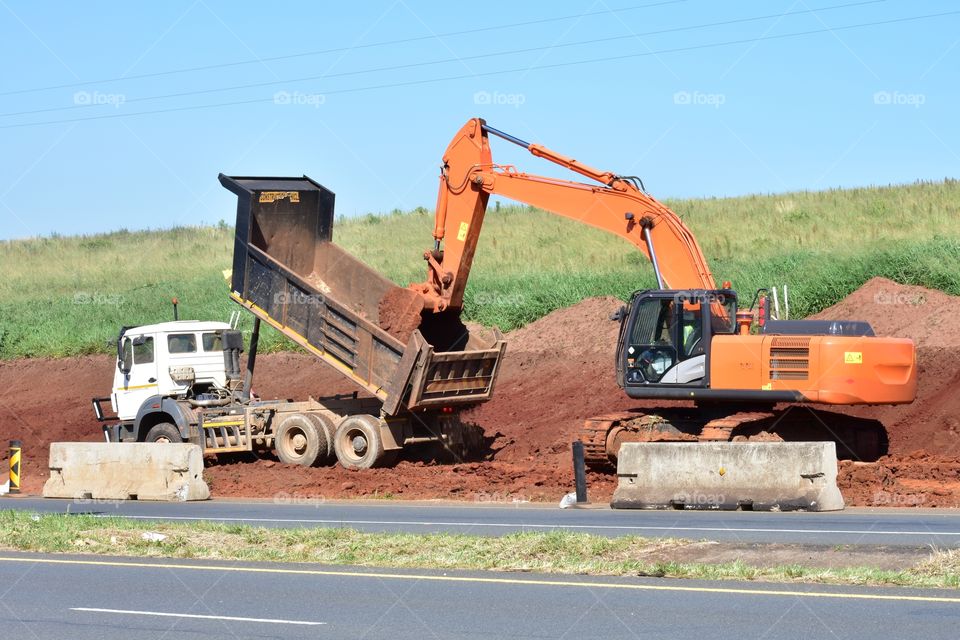 An Excavator Is Cleaning Sticky Soil From A Truck's Load-Bin