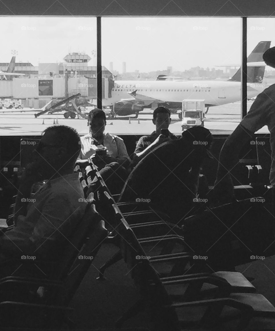Airport passengers, businessmen, waiting in Delta terminal lounge at New York LaGuardia with commuters and planes, black and white.