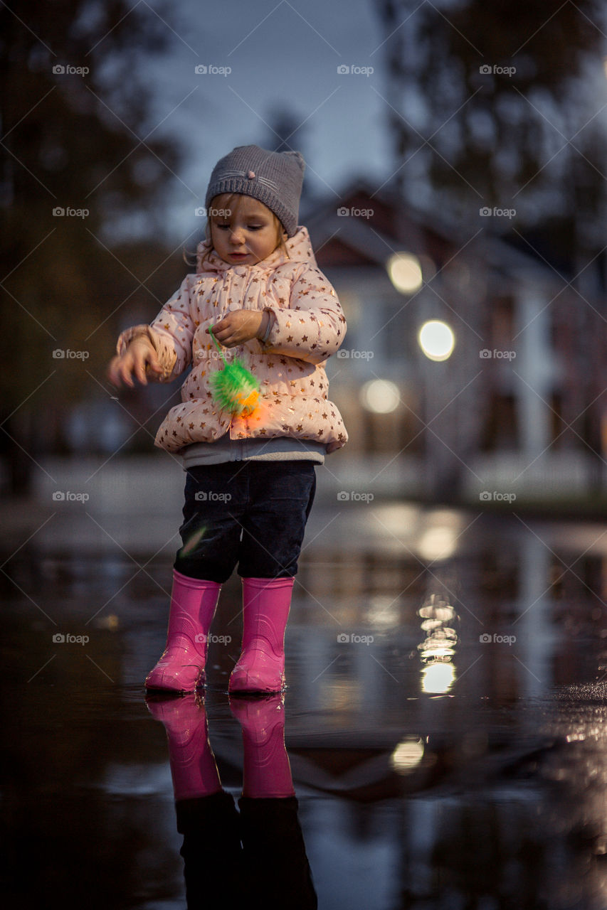 Little girl  in waterproof boots playing in a puddle 