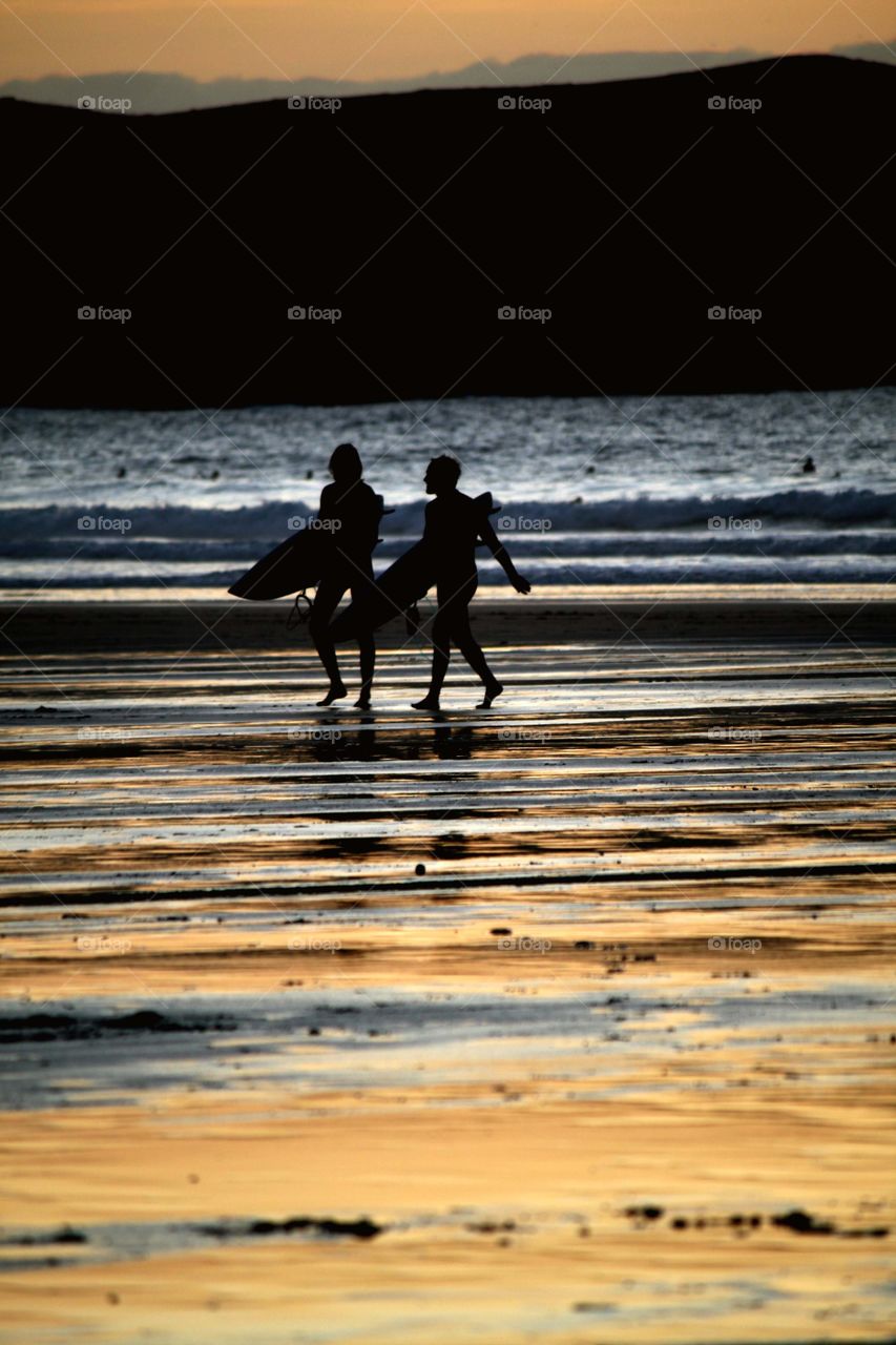 Surfer couple at sunset . A surfer couple on Fistral Beach in Cornwall at sunset, silhouettes agains the beautiful colourful reflections on sand 