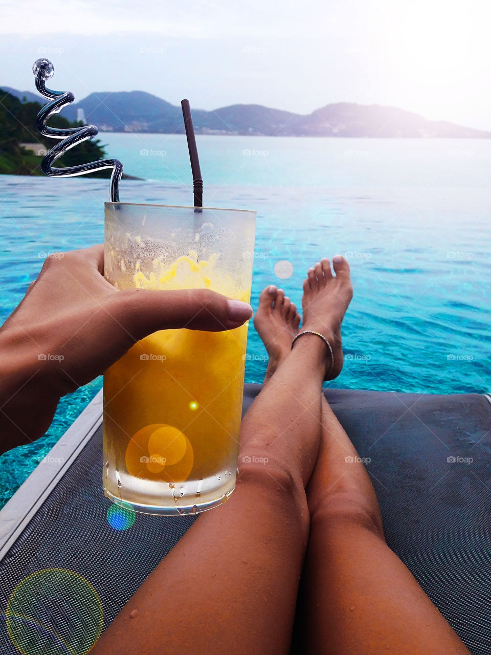 Young woman enjoying her summer tropical cocktail by the swimming pool over the ocean 