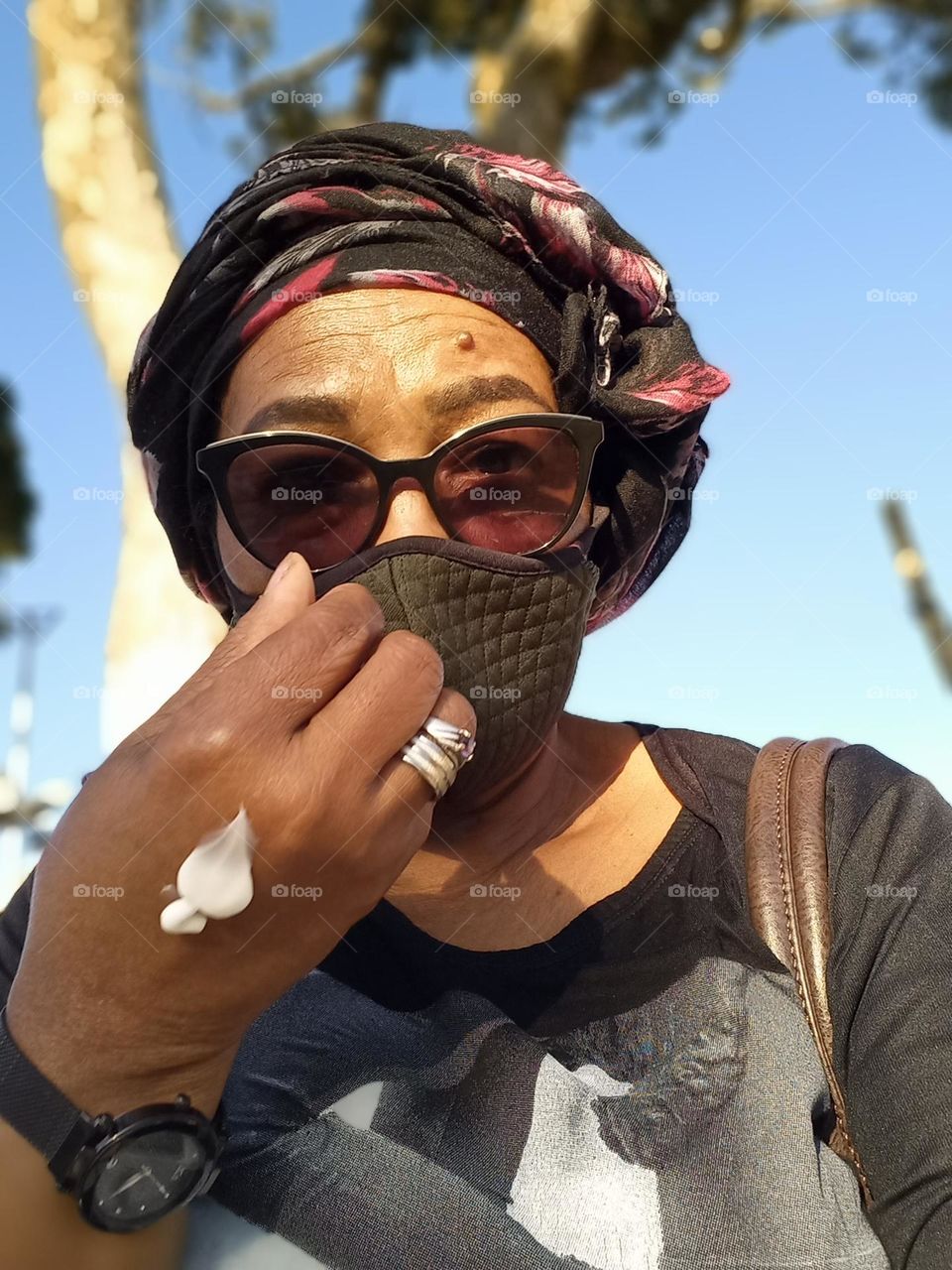 Senhora afrodescendente, usando máscara e um lenço na cabeça com creme nas mãos; preparando para sair