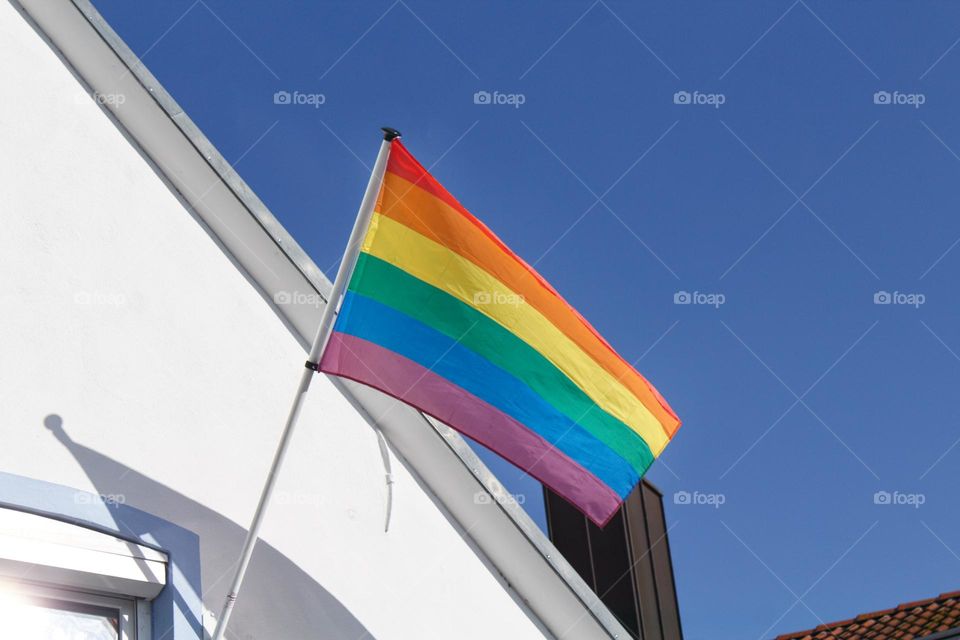 Rainbow flag for LGBTQ+ rights hanging out of the window of a house.