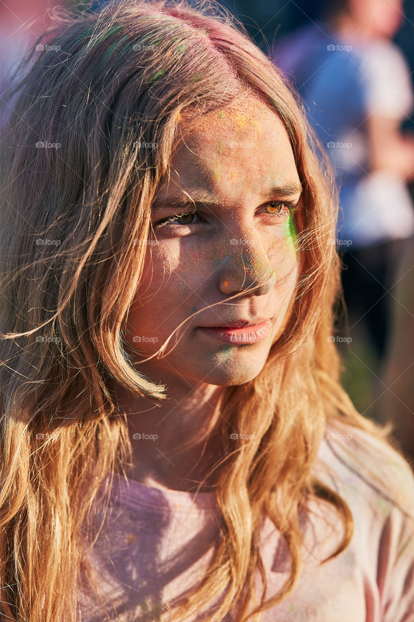 Portrait of happy smiling young girls with colorful paints on faces and clothes. Two friends spending time on holi color festival. Real people, authentic situations