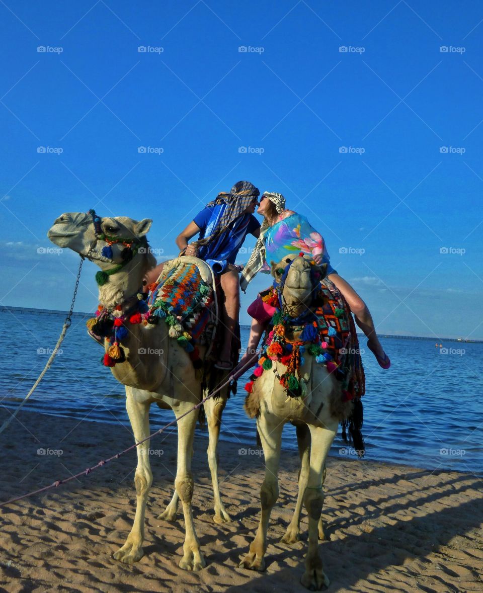 Tourist couple enjoying on camel ride at beach