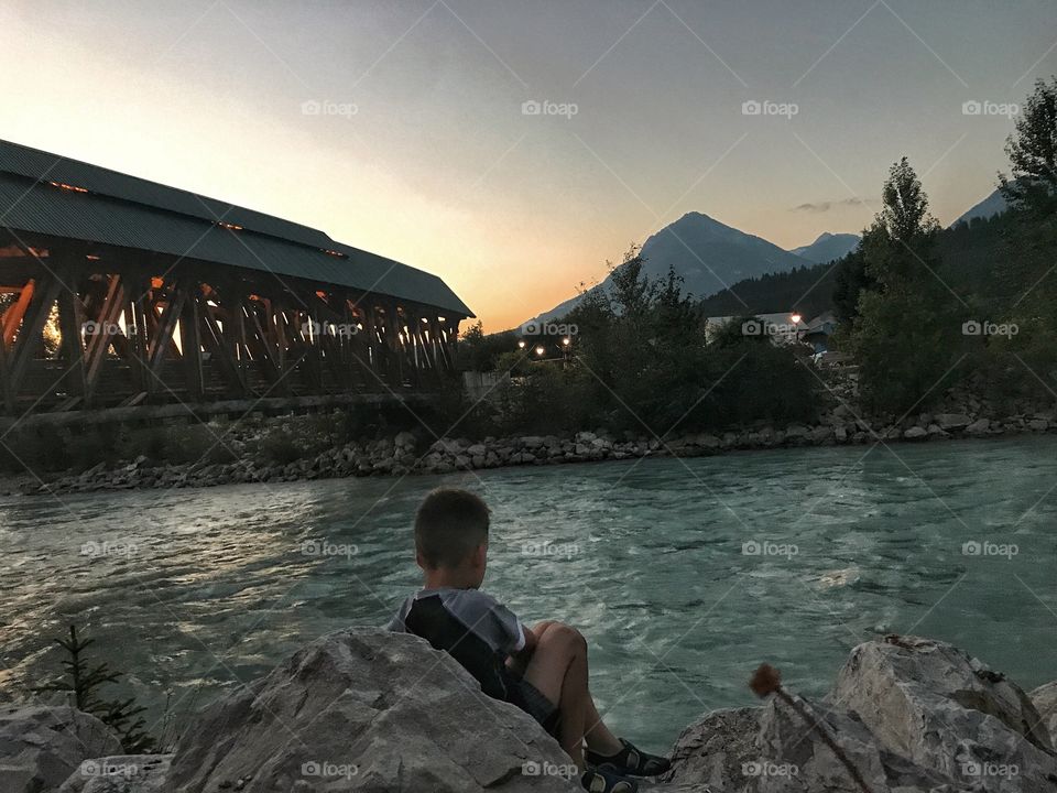 Beautiful Sunset scenery located in Golden, British Columbia. Such peacefulness if a boy throwing rocks at a river, facing the Kicking Horse river and the gorgeous summits of the Rocky Mountains. 