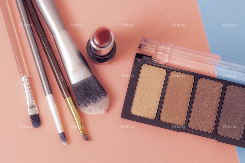 Nude eyeshadow palette, makeup brushes and red lipstick on a pink-blue background, flat lay close-up. The concept of female cosmetics, beauty salon.