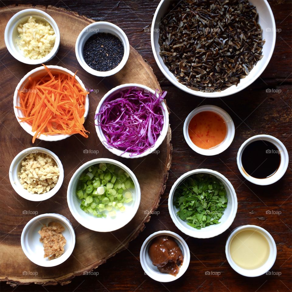 Ingredients for wild rice salad in white bowls on wood table. 