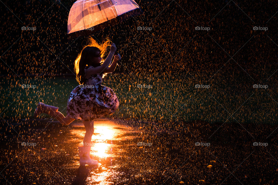 girl dancing in the rain with an bell with interesting orange back light