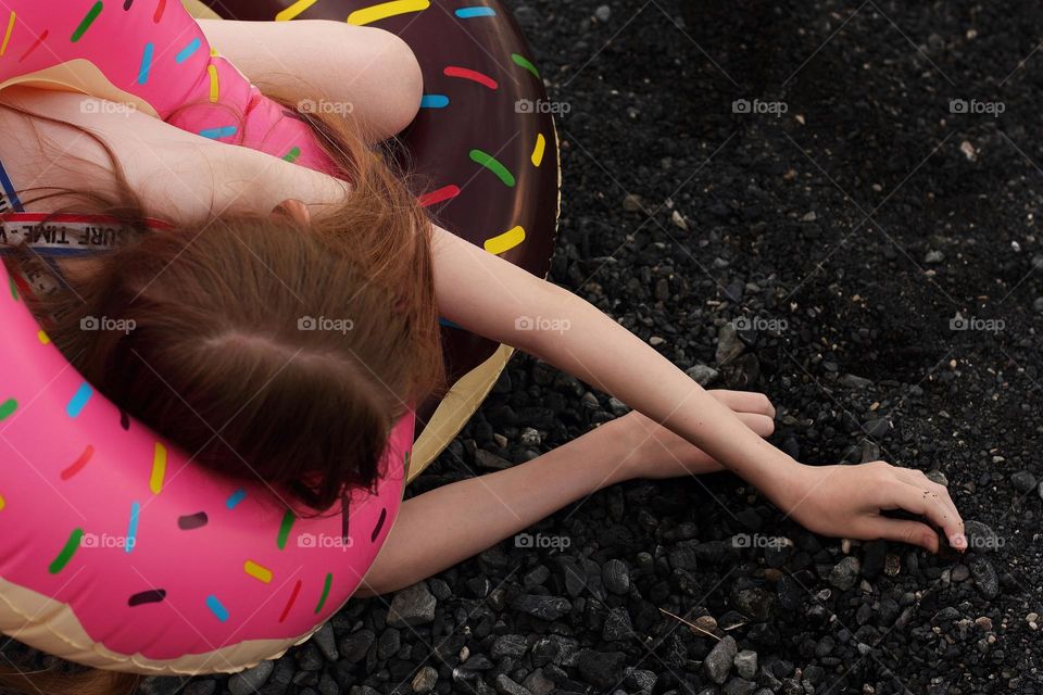 The girl stretching out her arms is resting on the black shore of the lake in inflatable circles - donuts