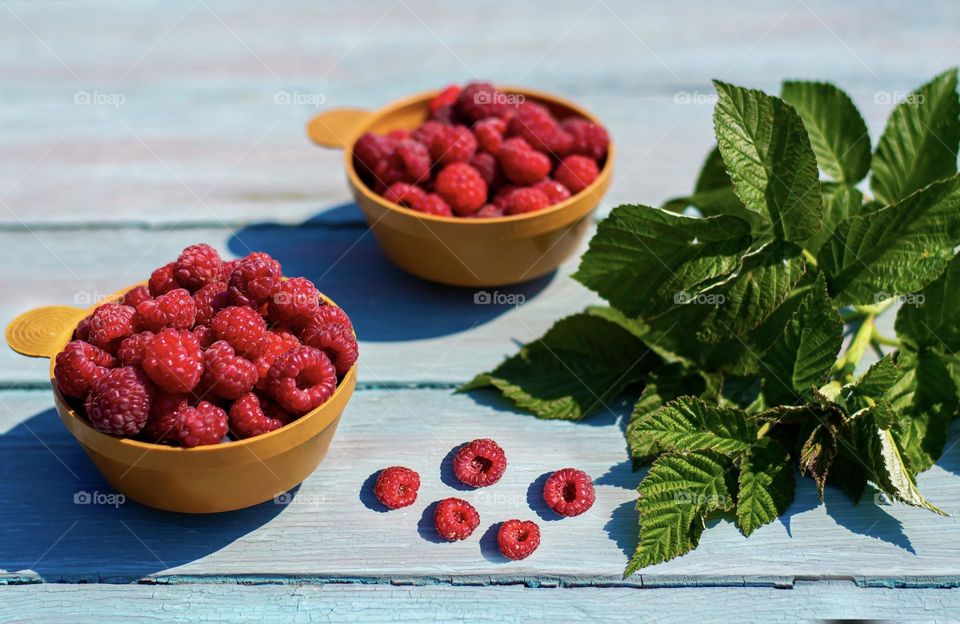 Summer food, fresh ripe raspberries in a cup. Delicious breakfast on blue wooden background