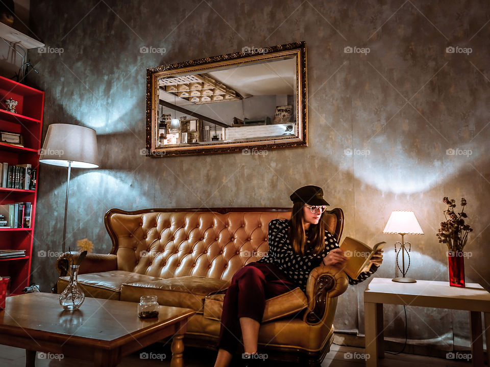 Young girl at the living room sat on the coach reading a book