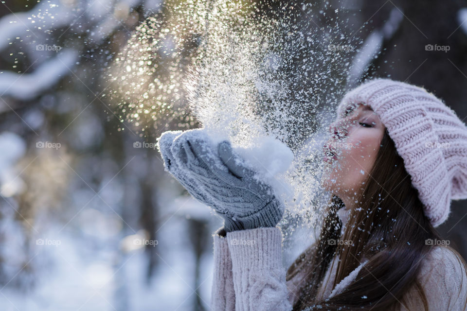 Woman blowing on snow in winter forest