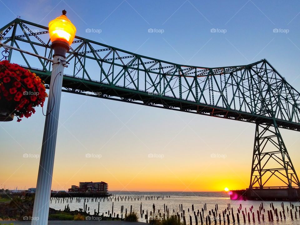 A natural light from a sunset in the horizon under a cantilever bridge with the lighted street lamp off to the side.