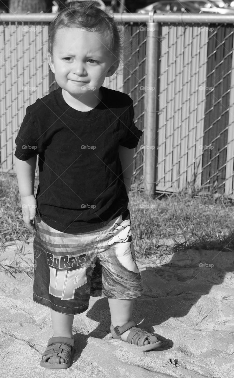 A cute little toddler boy hangs out and plays in the sand on a sunny summer day. 