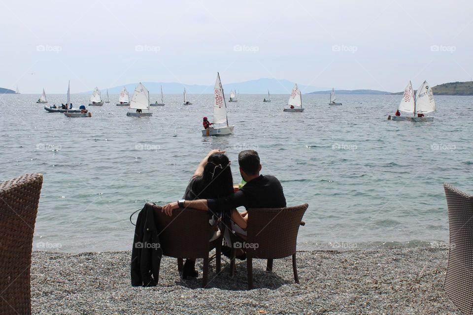 A couple enjoying their day in a coastline cafe with panoramic harbor and boats' views in Bodrum. 
