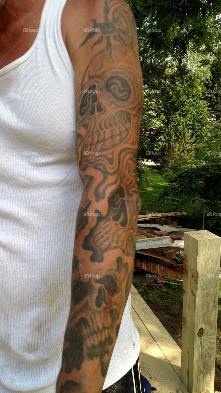 Sleeve tattoo of different skulls and a tribal sun