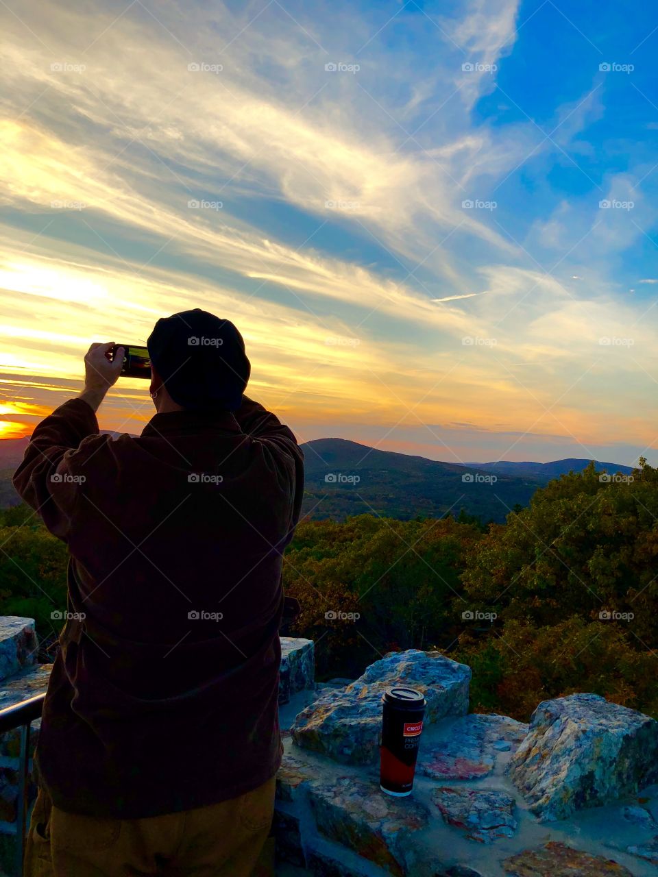 Mountain Sunset in Fall with a silhouetted man photographing the scenic view from atop a stone tower atop Mount Battie in Camden, Maine USA 