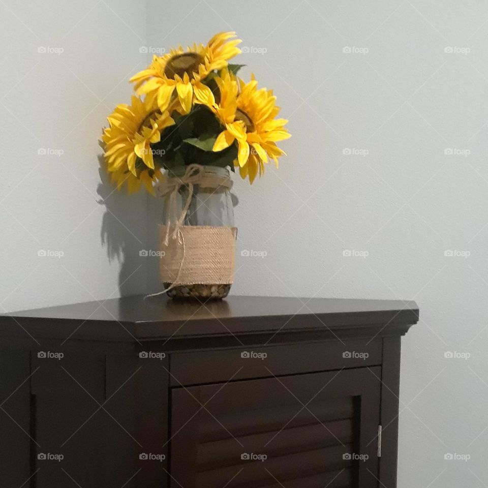 A bouquet of not real sunflowers sits in a vase that is atop a dresser in a bathroom.