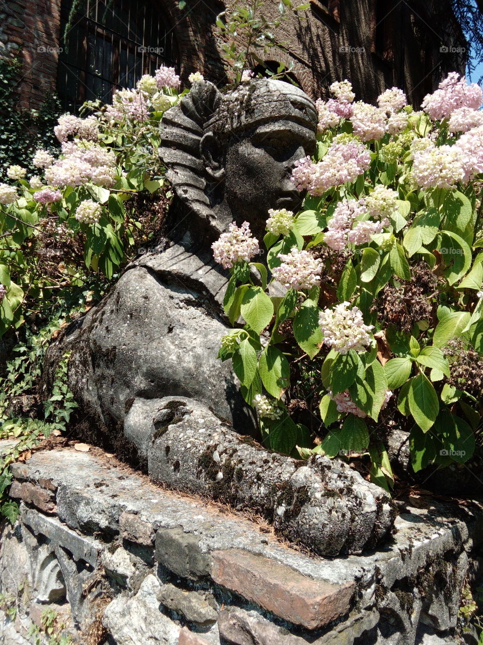 Reproduction of a sphinx statue in Italy, private park with flowers