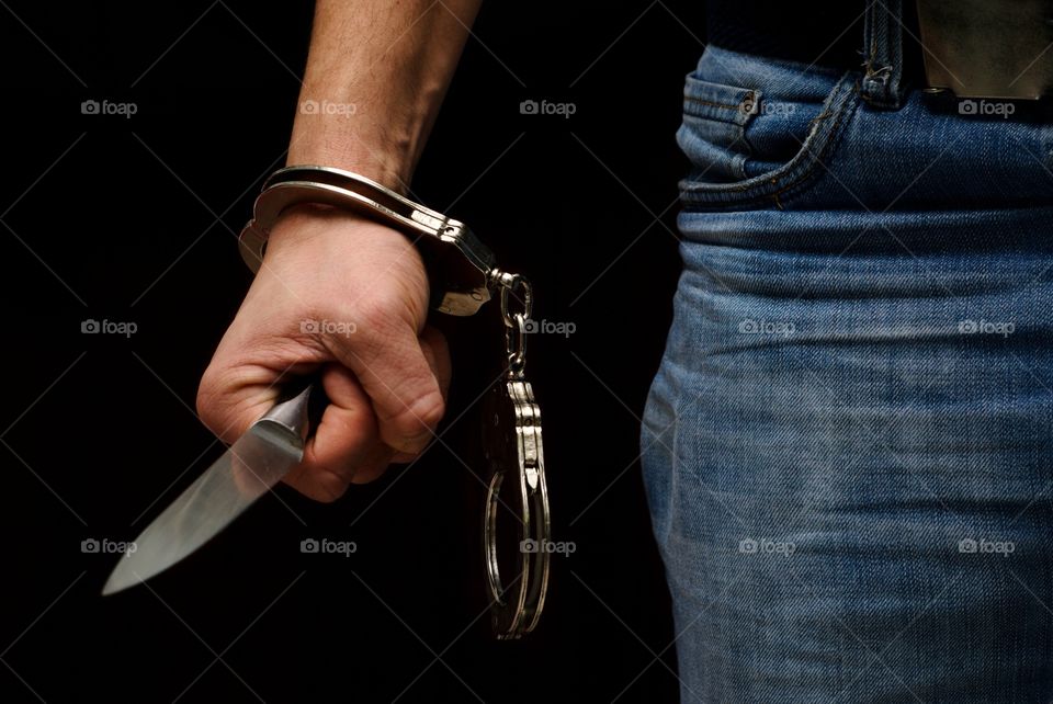 Hand with a knife and handcuffs on a black background