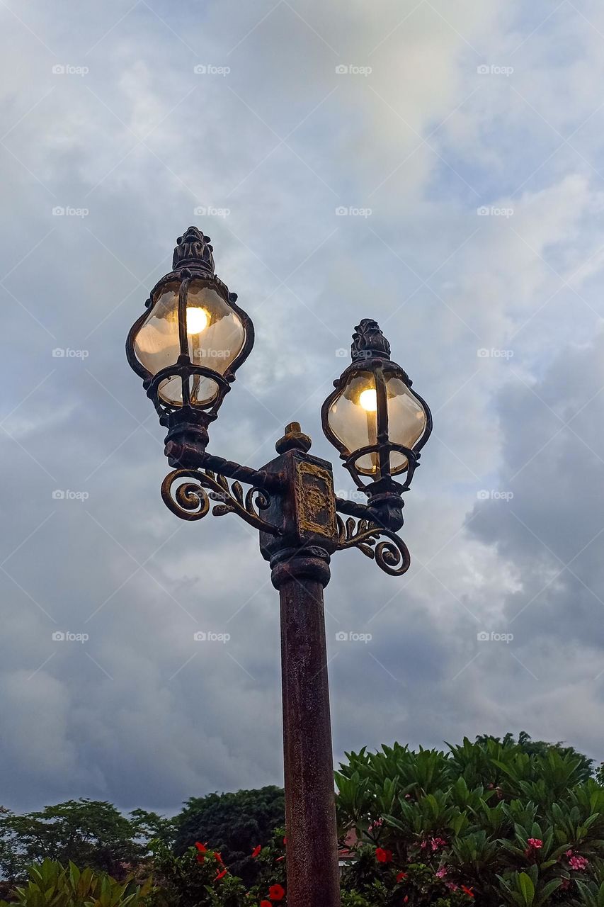 Low angle view of illuminated street light against cloudy sky