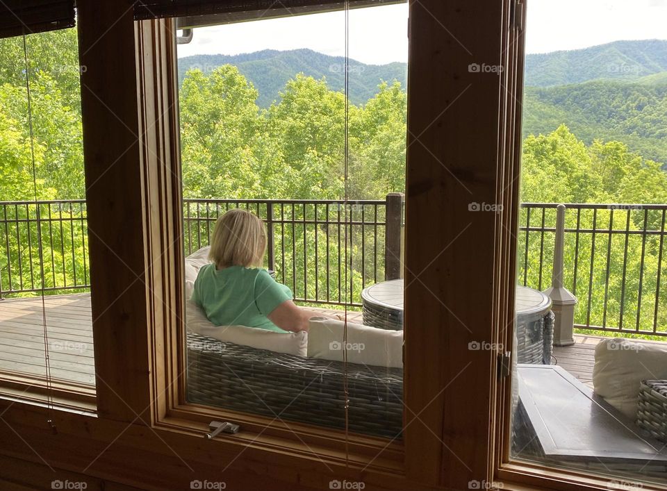 Woman sitting out on the deck seen through the window 