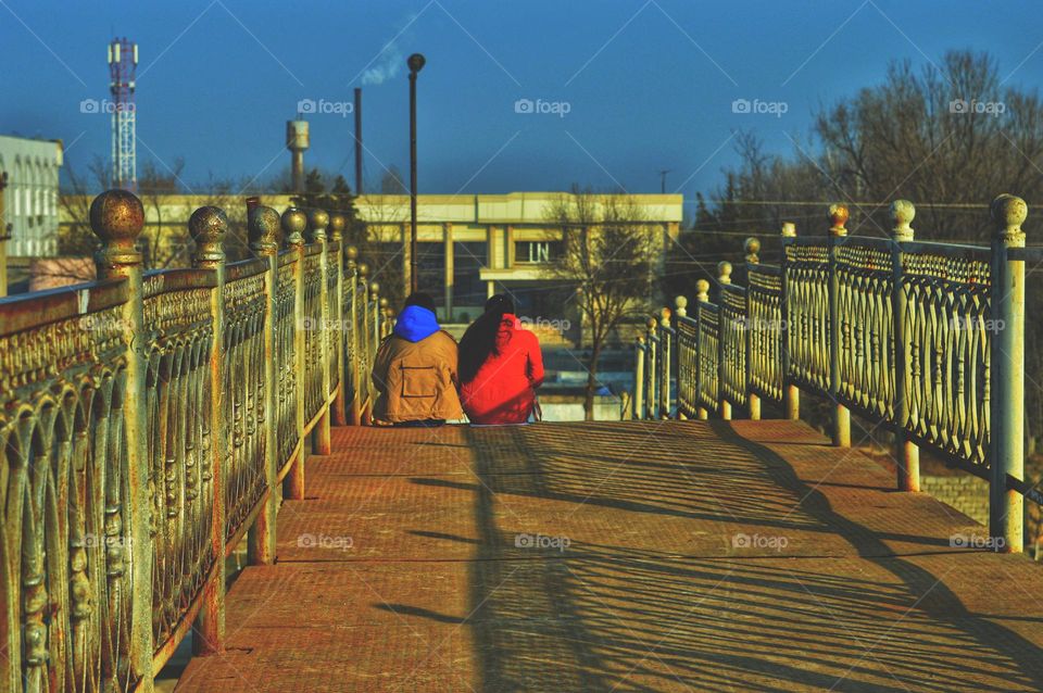 two friends sitting cuddled on a bridge