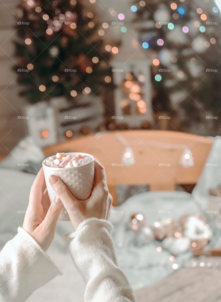 Cup with marshmallows in female hands on a background of Christmas decor