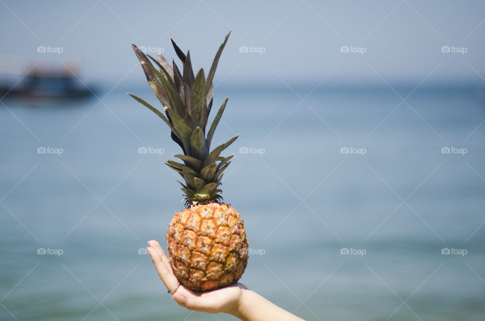 Woman holding a pineapple against the sea water 
