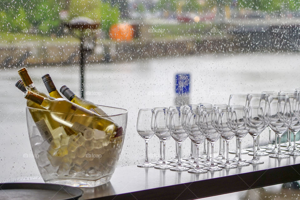 wine bottles in bowl with ice cubes and many glasses on a rainy window background