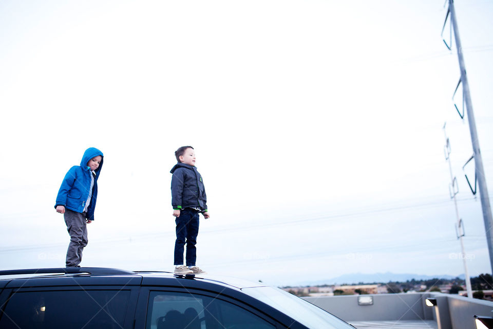 Boys watching sunrise by standing on a car in a parking garage 