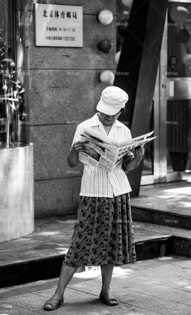 Asia China old woman read newspaper on the steet. black and white