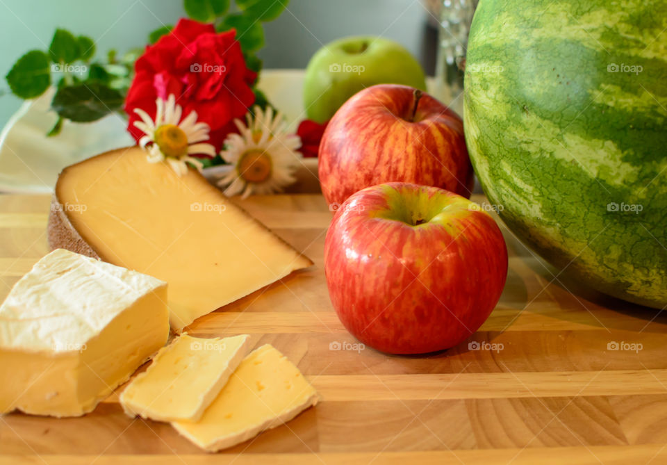 Row of red and green fresh sweet apples on wood table with daisy flowers, watermelon  and sliced cheese 