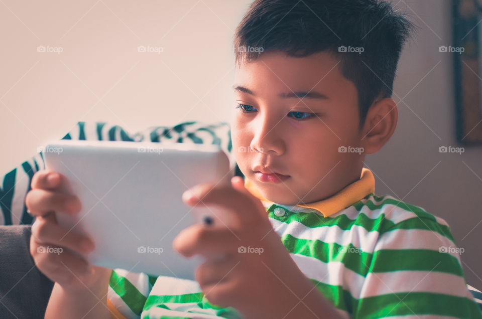 A boy using his tablet playing or watching a movie.