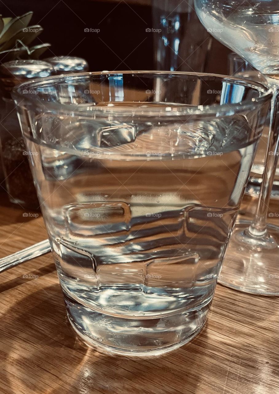 The reflection of silver fork times in a glass of water, on a dining room table. 