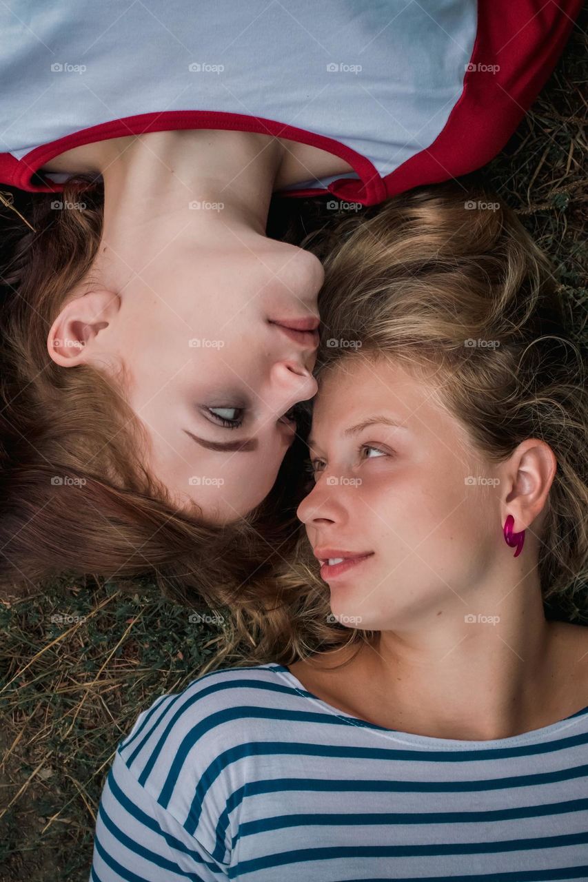 Two women laying down looking into each other s eyes, smiling