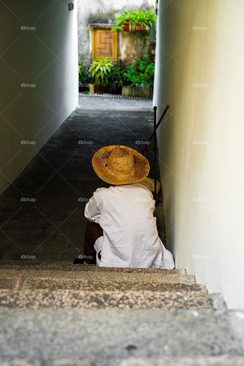 Life isn't fair to everyone. An old man is resting in a small Shadow. A hat on his head shows that he is not in his comfort zone all the times whenever he needs to move around.