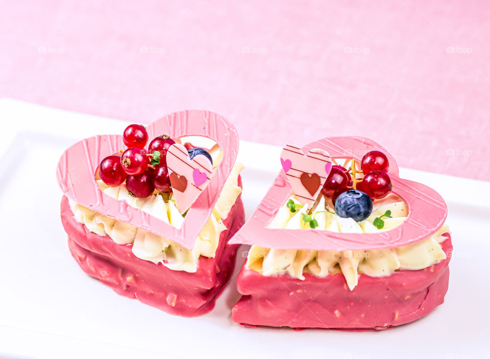 Two cakes with almond flour, chocolate and fresh berry in heart shape on white plate at pink background.