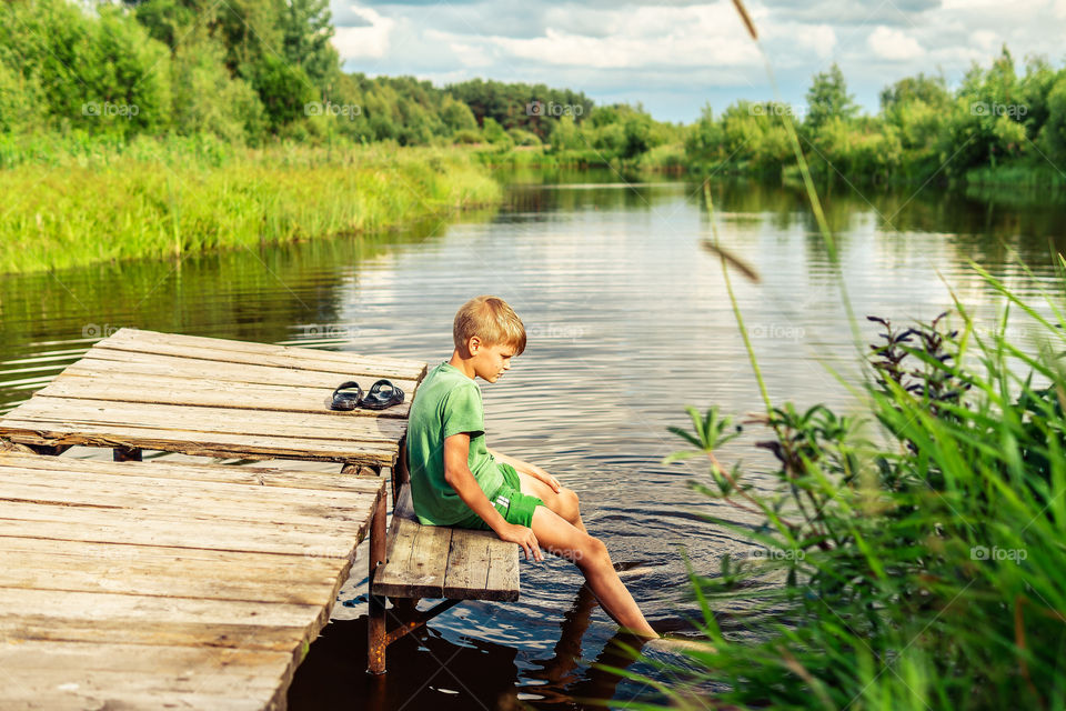 Boy is sitting and relaxing near the water in the village