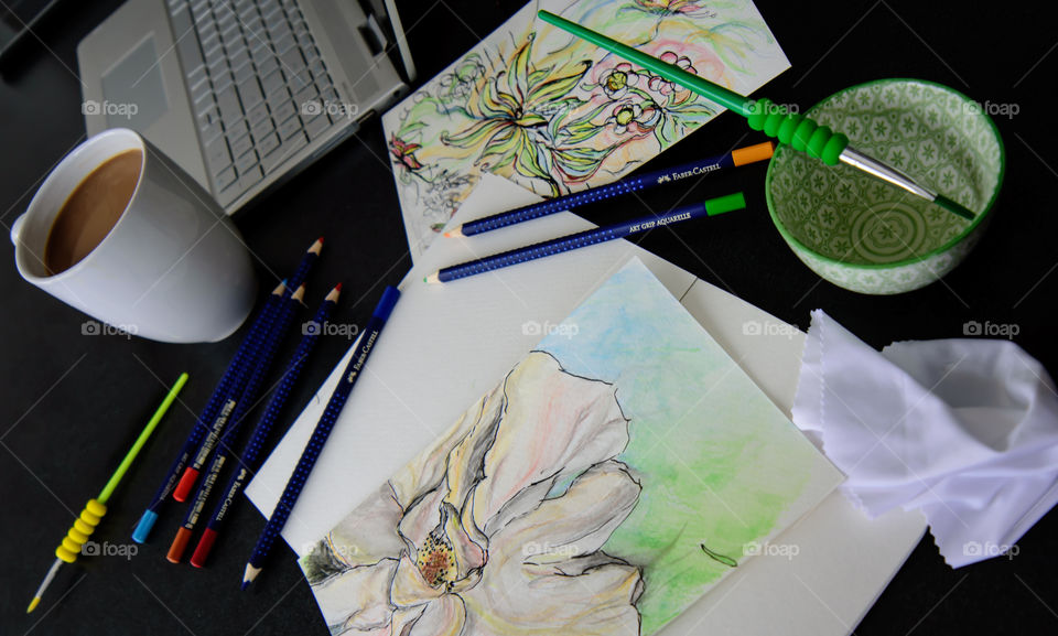 High angle view of Desk with Floral spring creative sketches, coffee, laptop and art tools Sketching with Faber-Castell PITT Artist pens and aquarelle pencils using watercolor techniques 
