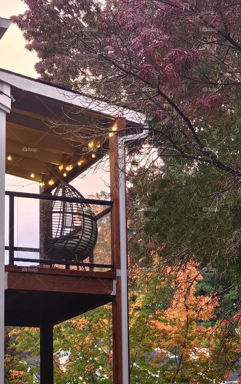 An Oregon apartment deck decorated with lights against a background of Autumn trees at sunset