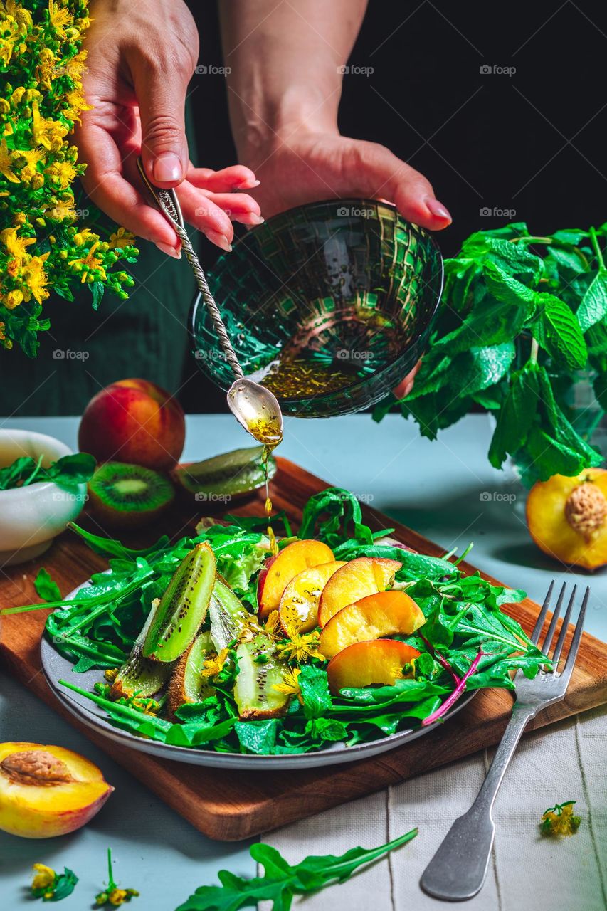 the girl prepares a bright summer salad of peaches, kiwi, arugula, and fragrant oil - vitamin mood, healthy lifestyle and delicious food. Diet and rational nutrition