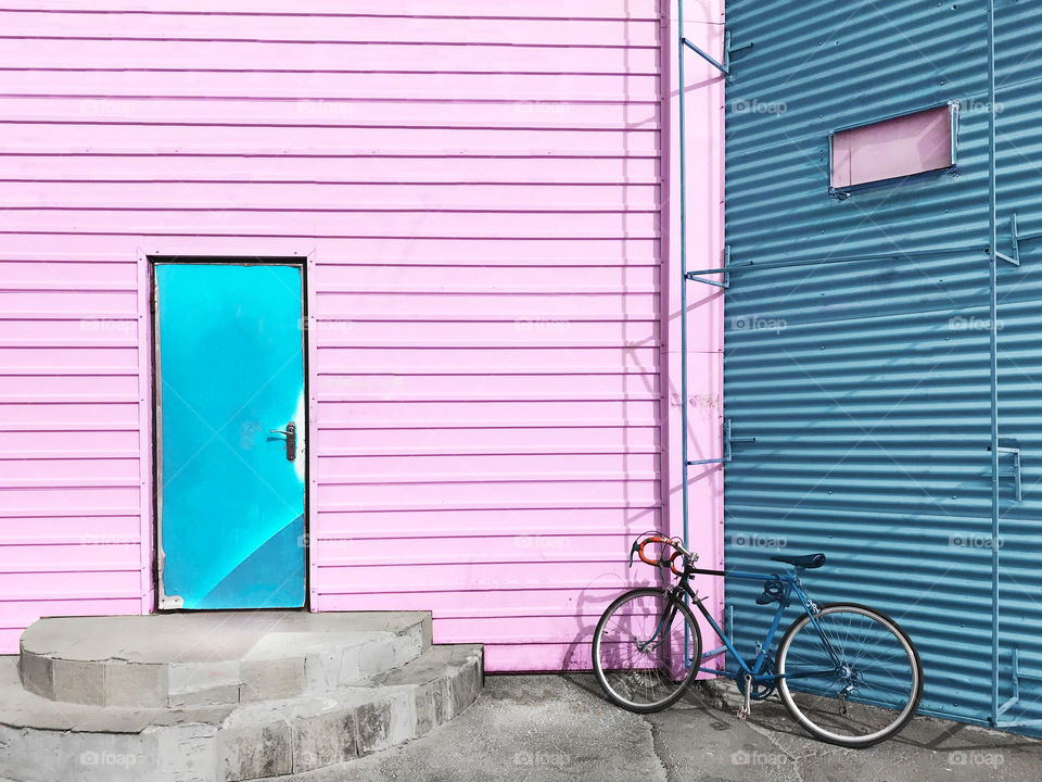 Bicycle standing on the city street in front of geometric pink and blue pastel wall with blue door 