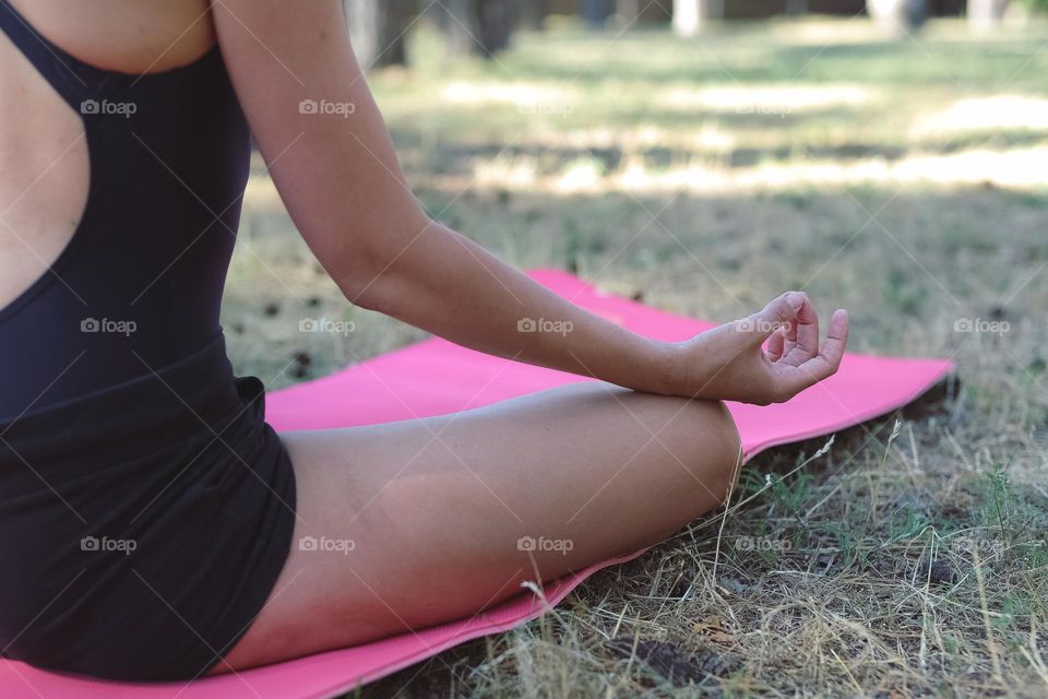 a girl in a black tracksuit, on a pink rug in the forest, does yoga, the girl meditates