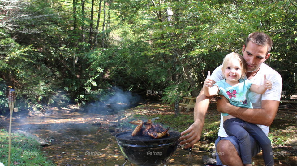 Dad holding daughter and grilling